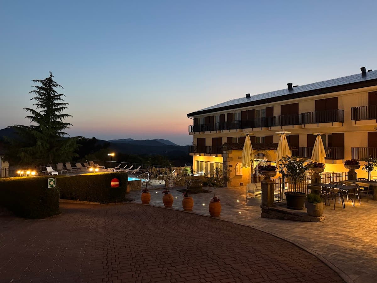Hotel exterior with illuminated patio, pool, and rolling hills at dusk
