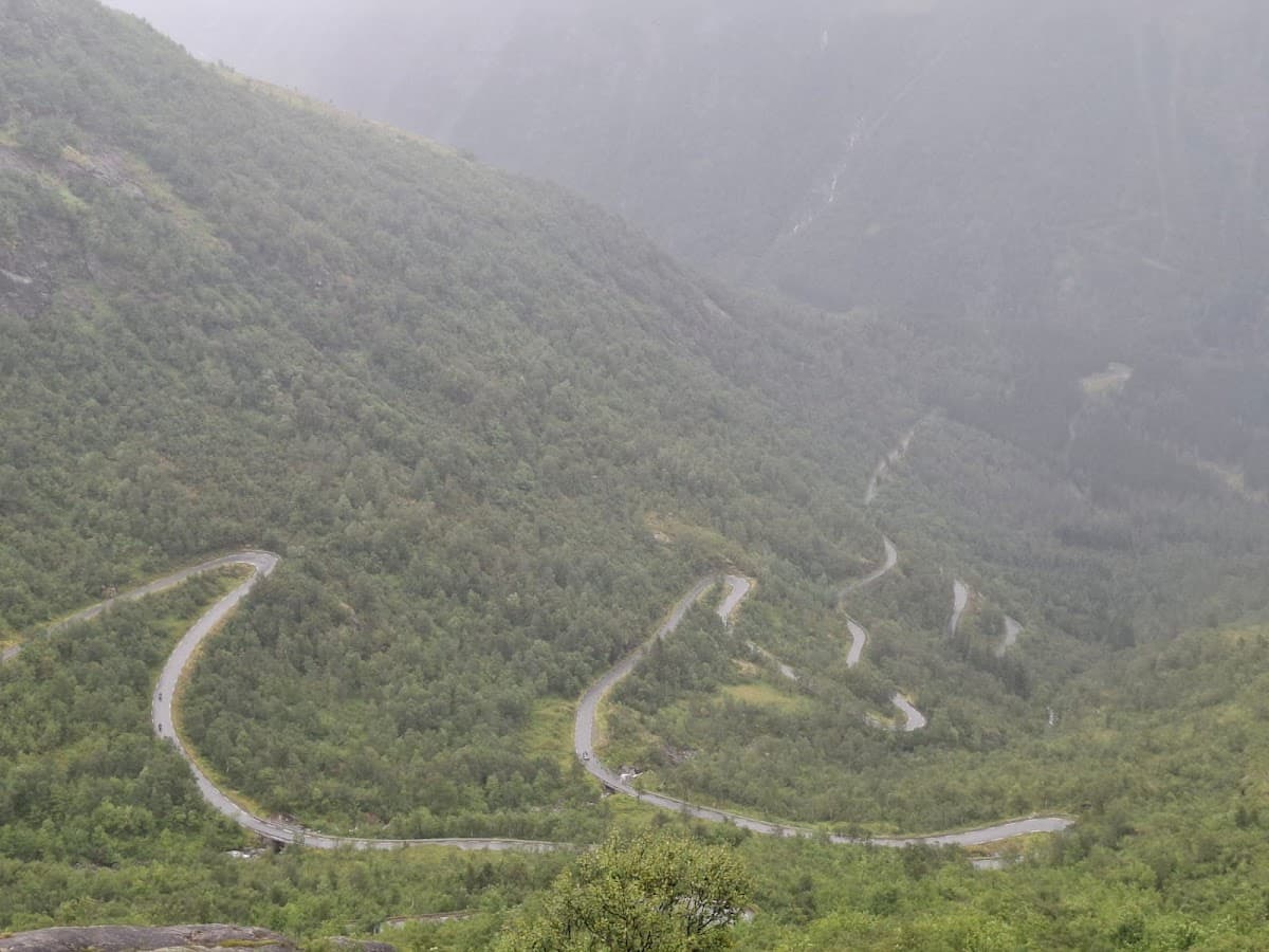Winding mountain road with switchbacks through dense green forest under foggy conditions