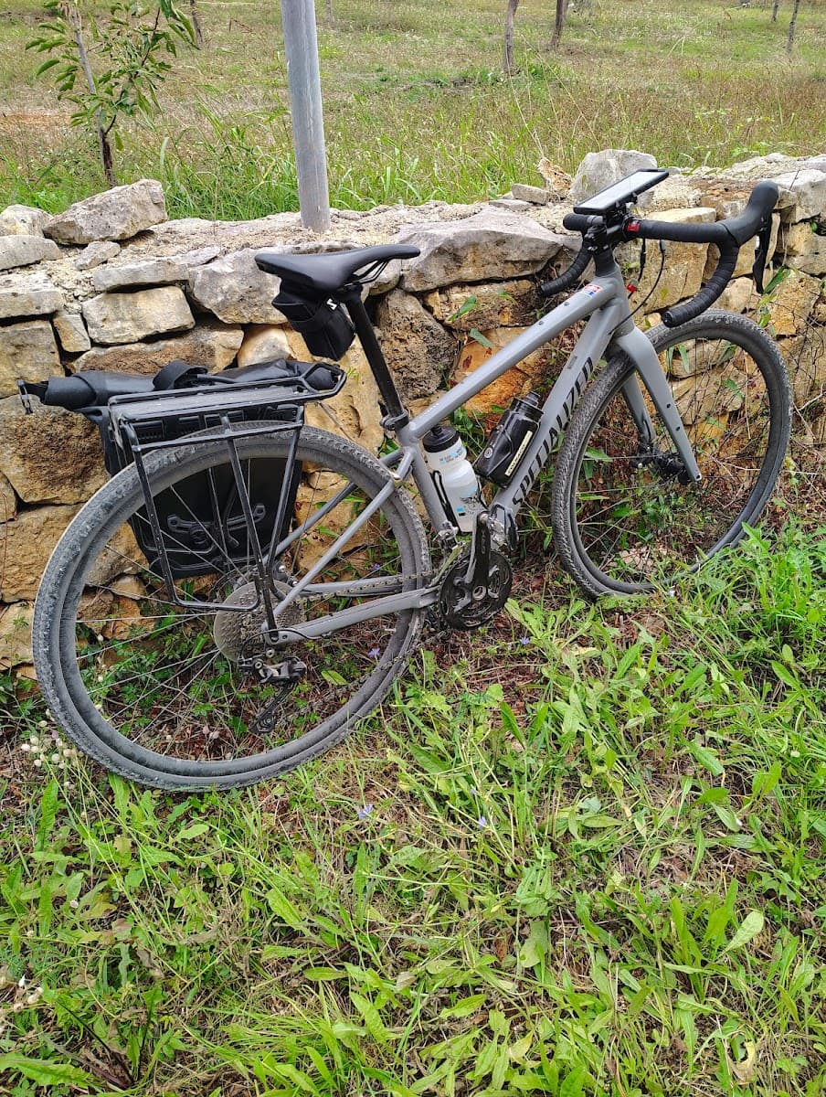Gravel bike with rear rack and phone mount resting against a dry-stacked stone wall outdoors.