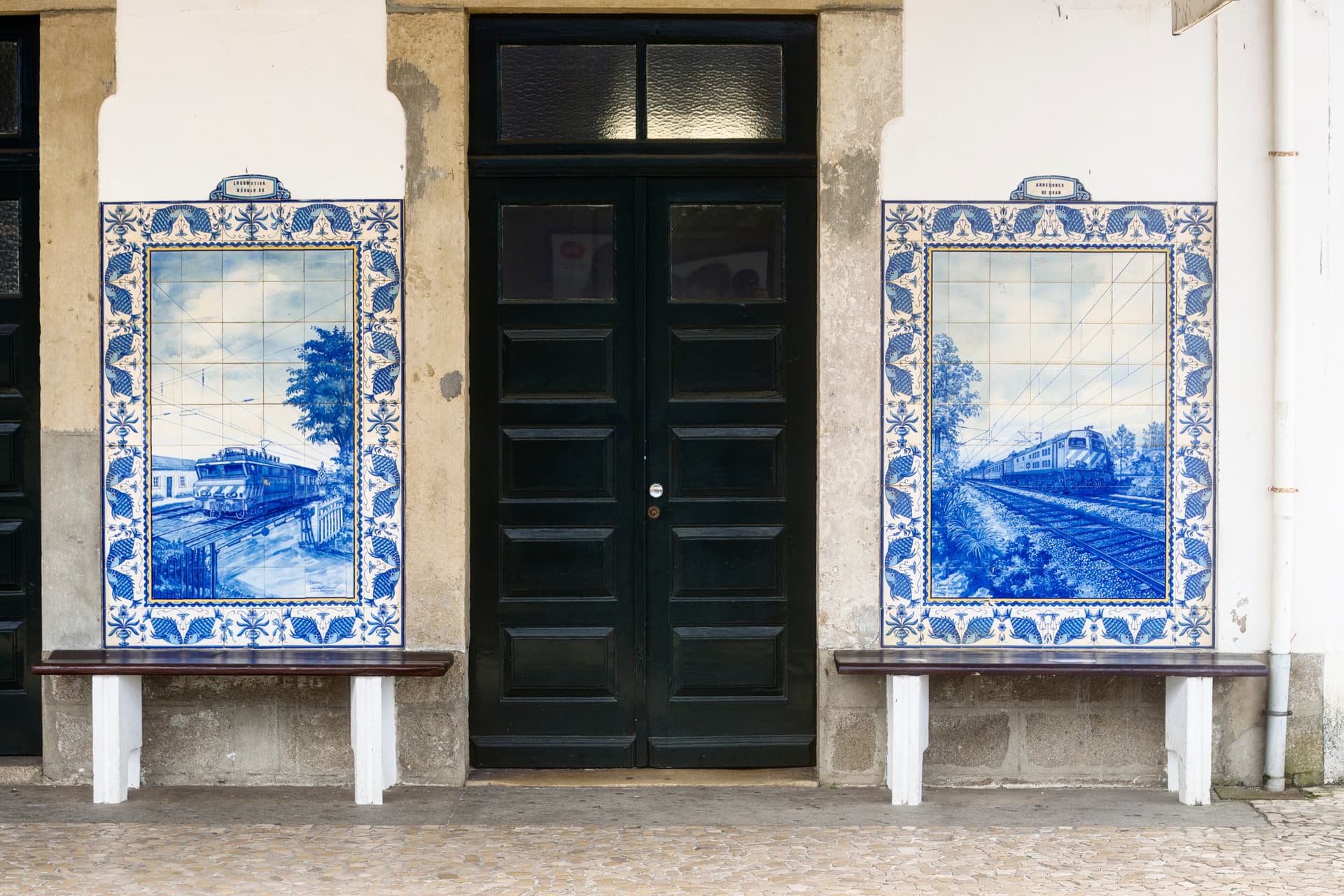 Azulejo tiles depicting trains flank a dark wooden door at Ovar, Portugal train station.