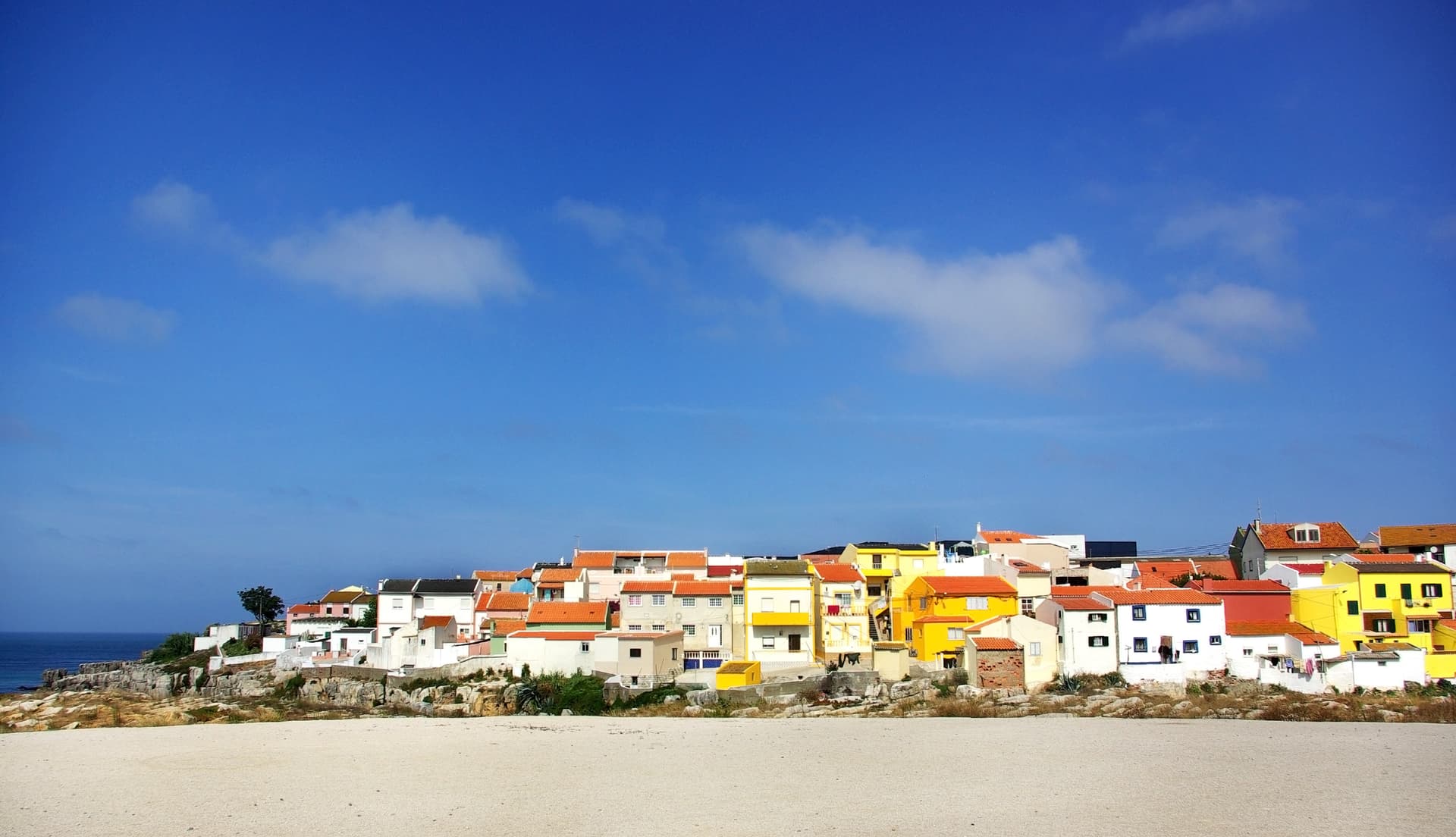 Colorful coastal village houses above sandy foreground and blue sea in Peniche.