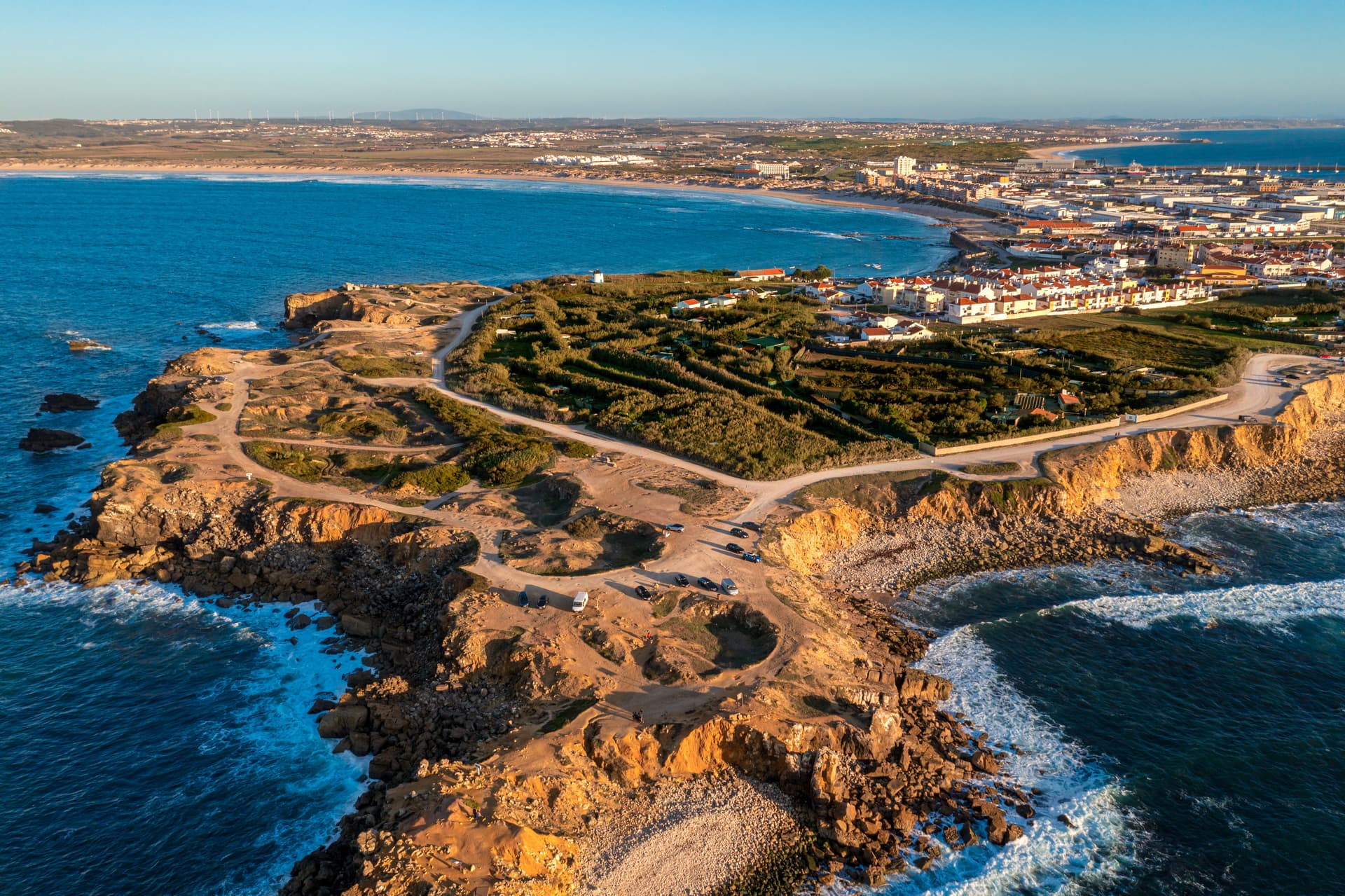 Aerial view of Peniche peninsula with rugged cliffs, coastal town, and blue ocean waves.