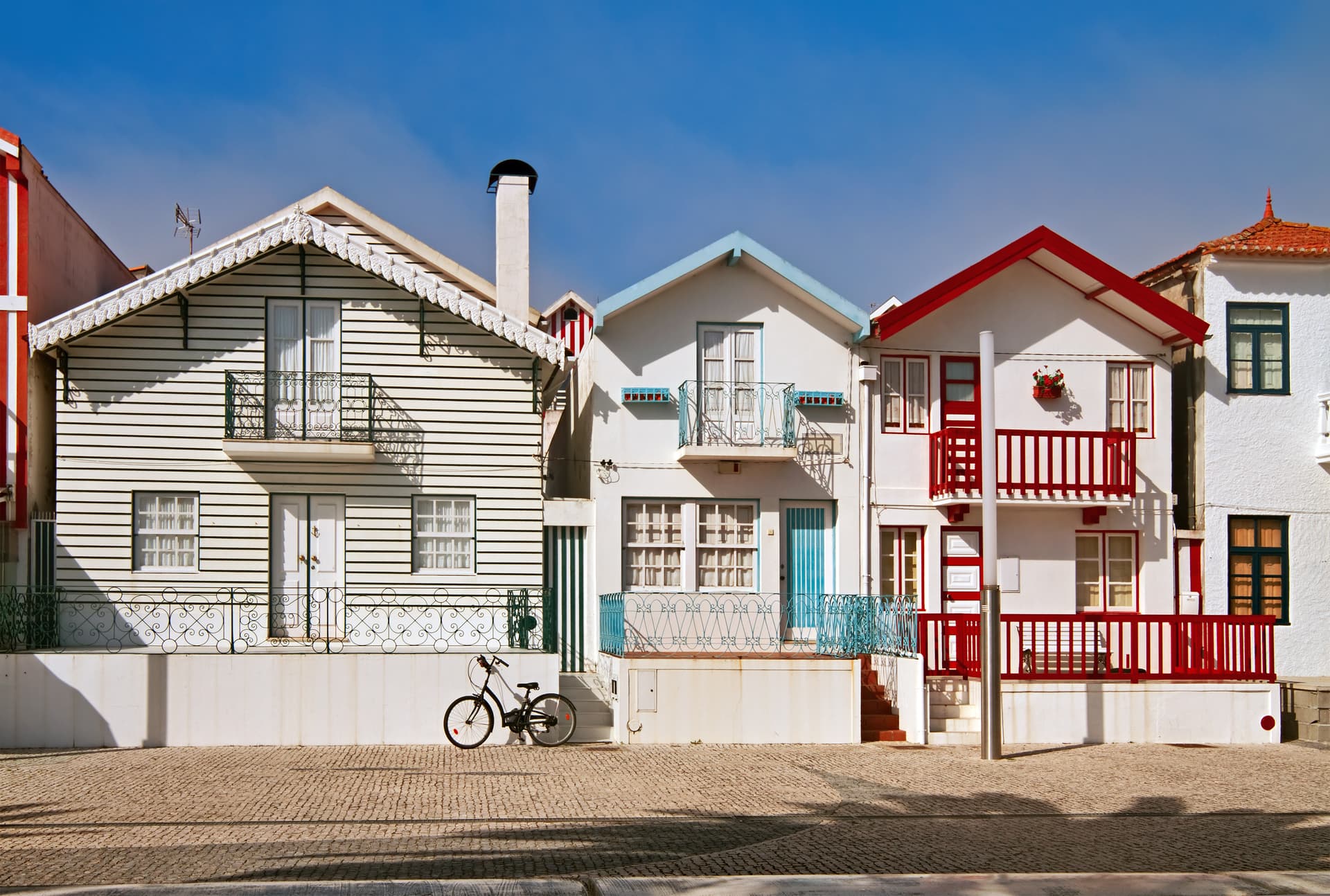 Bicycle parked on cobblestone street in front of colorful striped houses in Costa Nova.