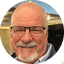 Close-up portrait of a smiling older man with glasses, graying hair, and a goatee.