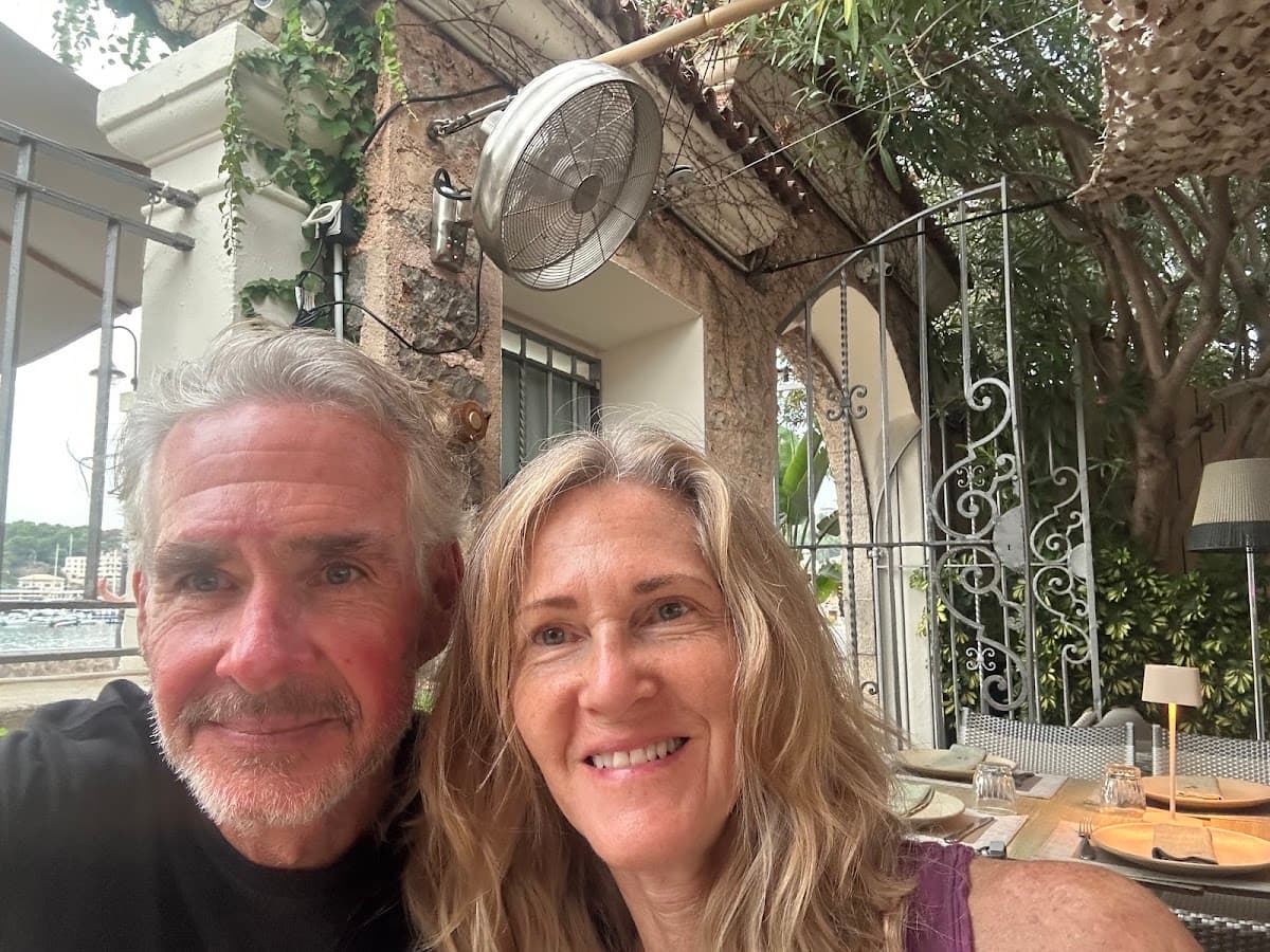 Couple taking a selfie at an outdoor restaurant terrace with stone walls and foliage