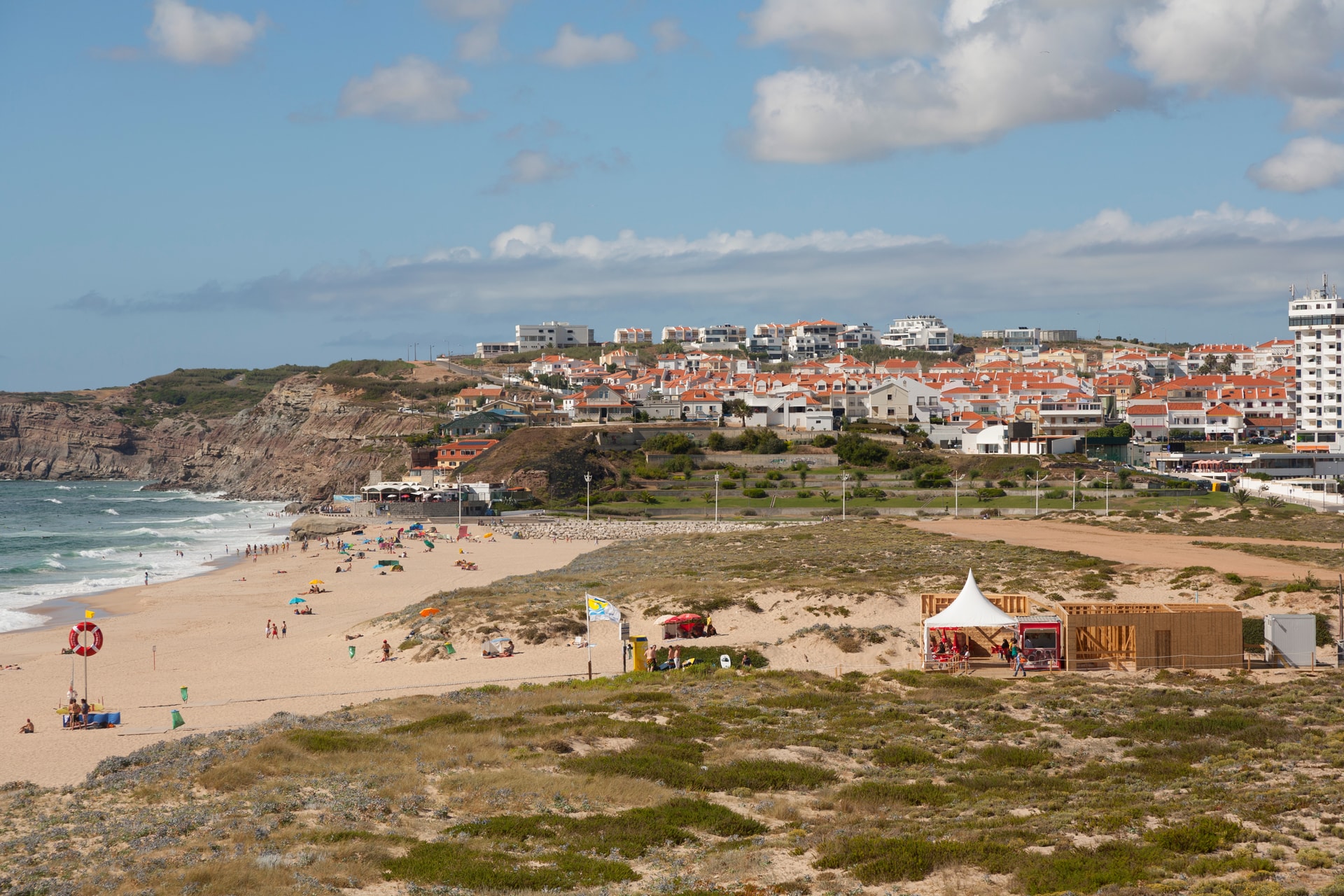 Beachgoers at Praia da Areia Branca with white buildings on coastal cliffs.
