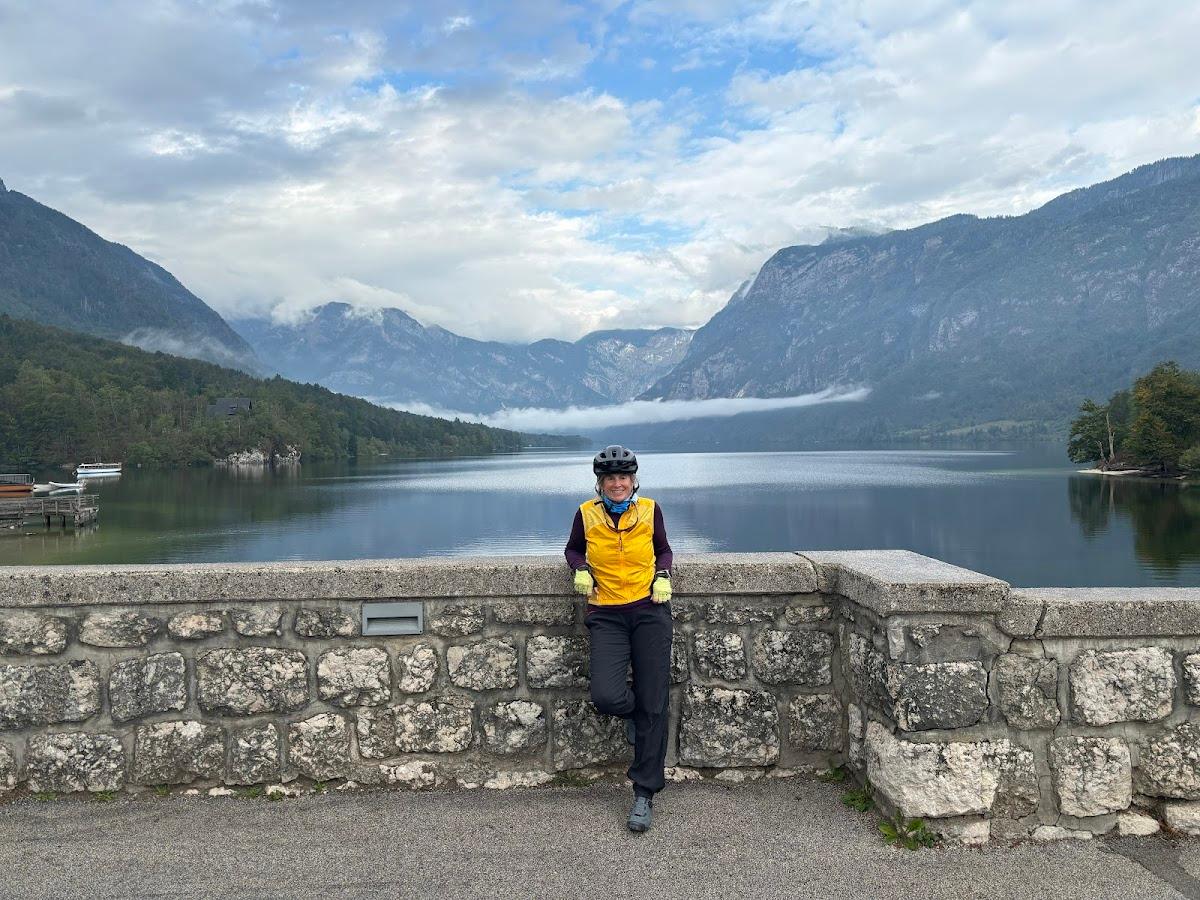 Cyclist leaning on stone wall overlooking calm lake surrounded by steep, forested mountains