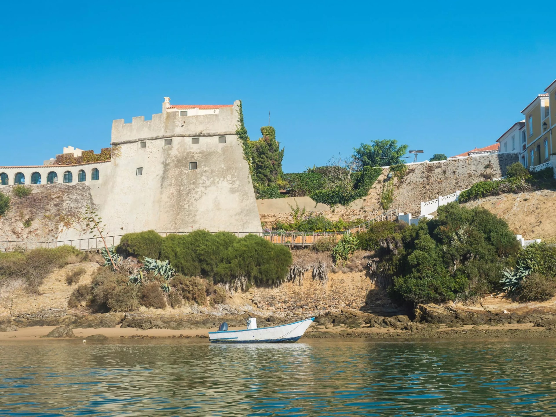 View of medieval fort Forte de Sao Clemente over the Mira river with small boat in sunny day with clear blue sky. Vila Nova de Milfontes, Portugal, Rota Vicentina coast