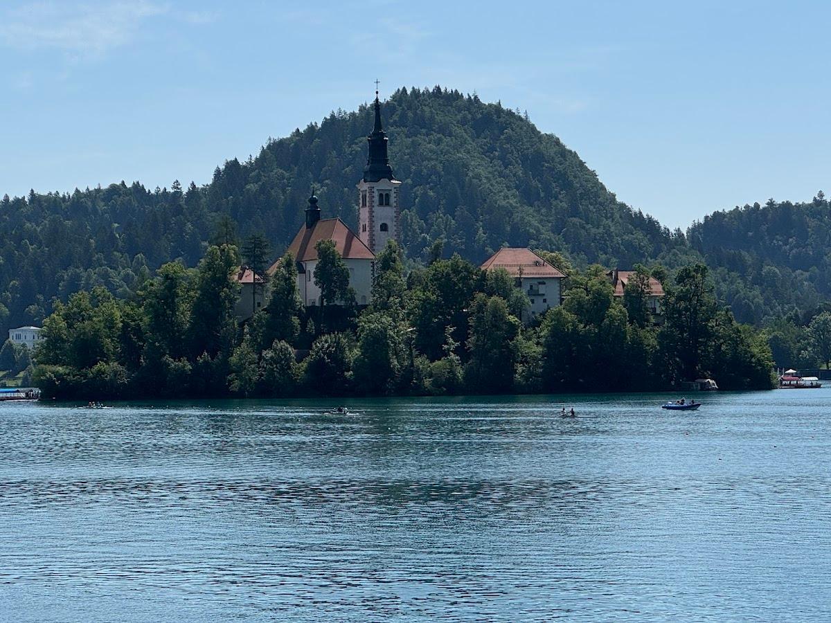 Church on island in Lake Bled with forested hill background and boats on water