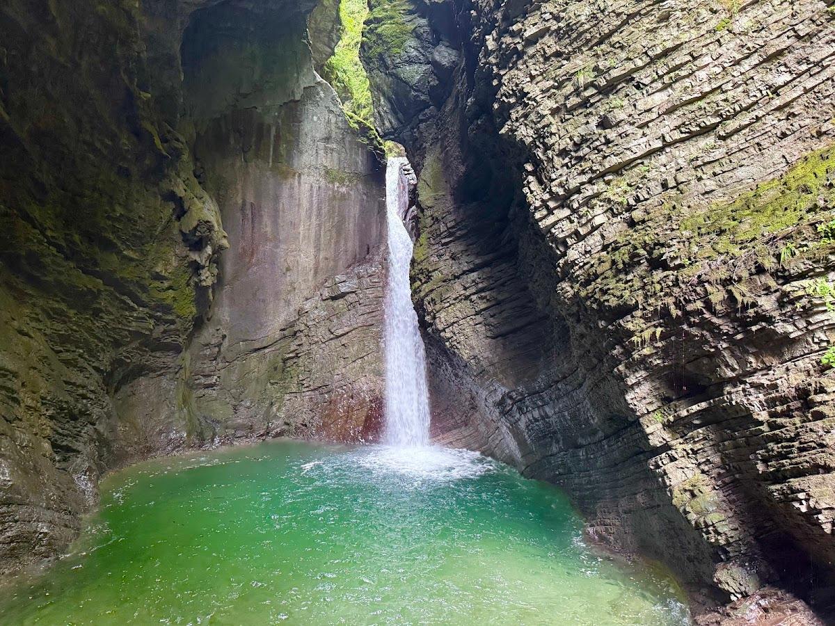 Waterfall plunging into a bright green pool in a narrow, moss-covered rock canyon