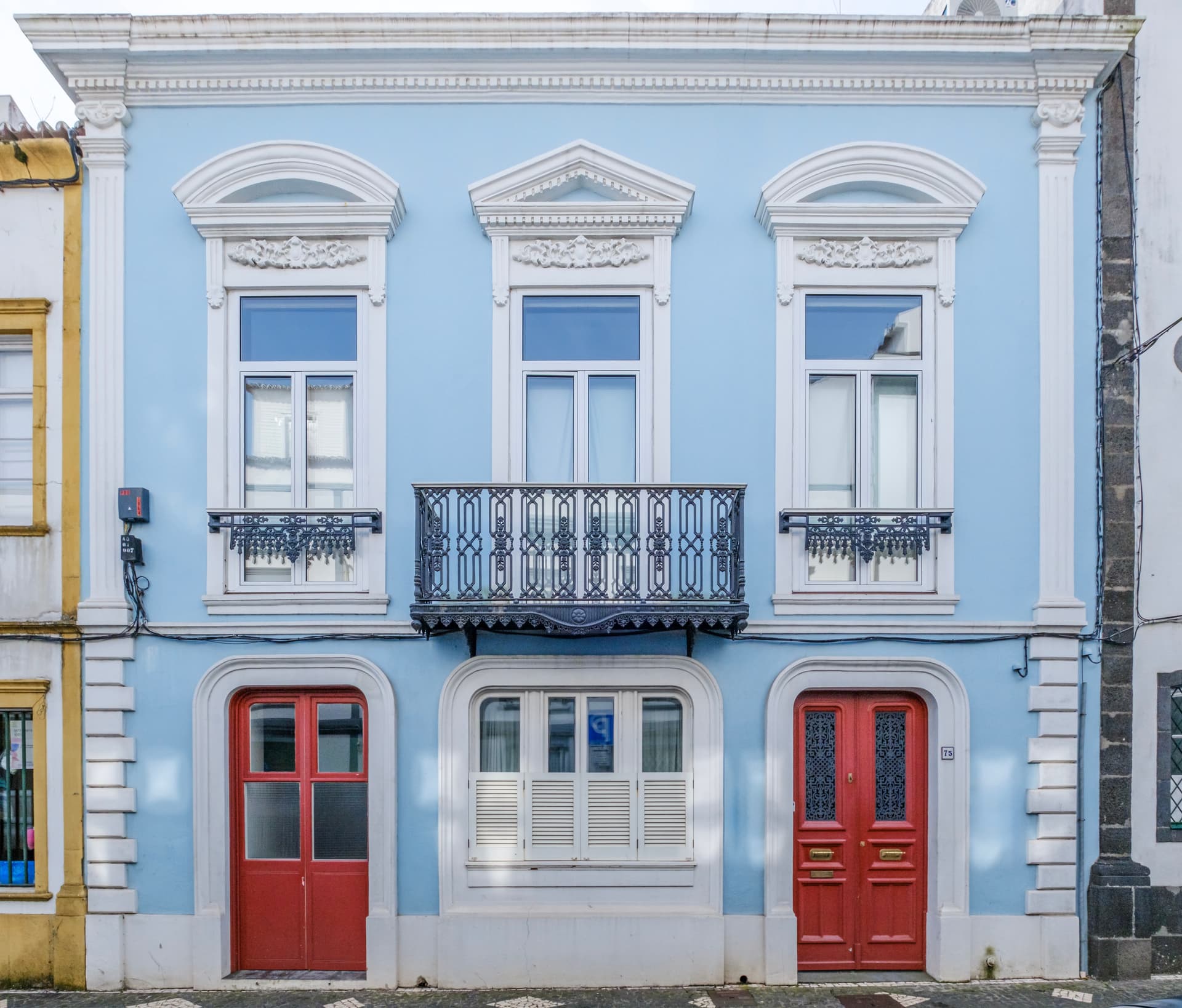 Light blue townhouse facade in Ponta Delgada with ornate white trim, red doors, and iron balcony.