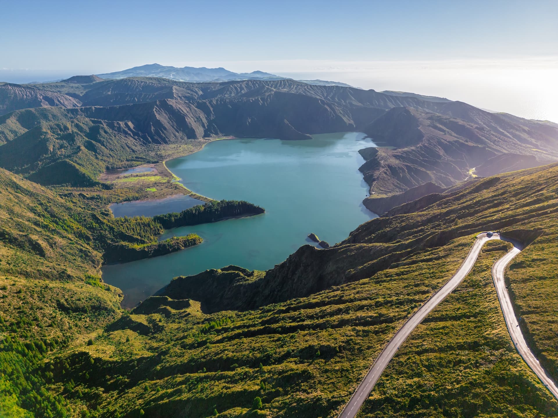Lagoa do Fogo crater lake with winding road on green, grassy hillside mountains.
