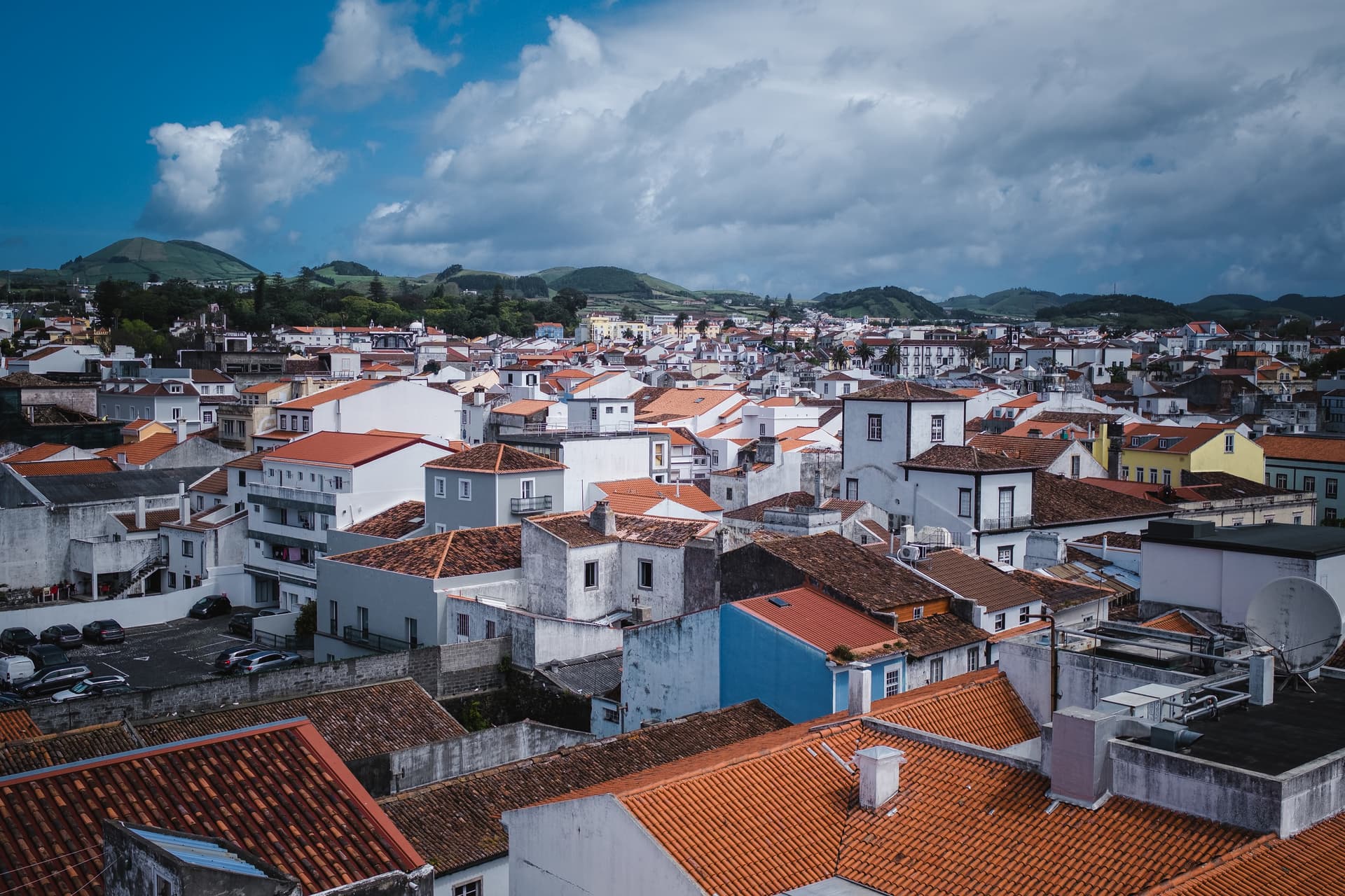 Rooftops in the center of Ponta Delgada with green hills under a cloudy blue sky.