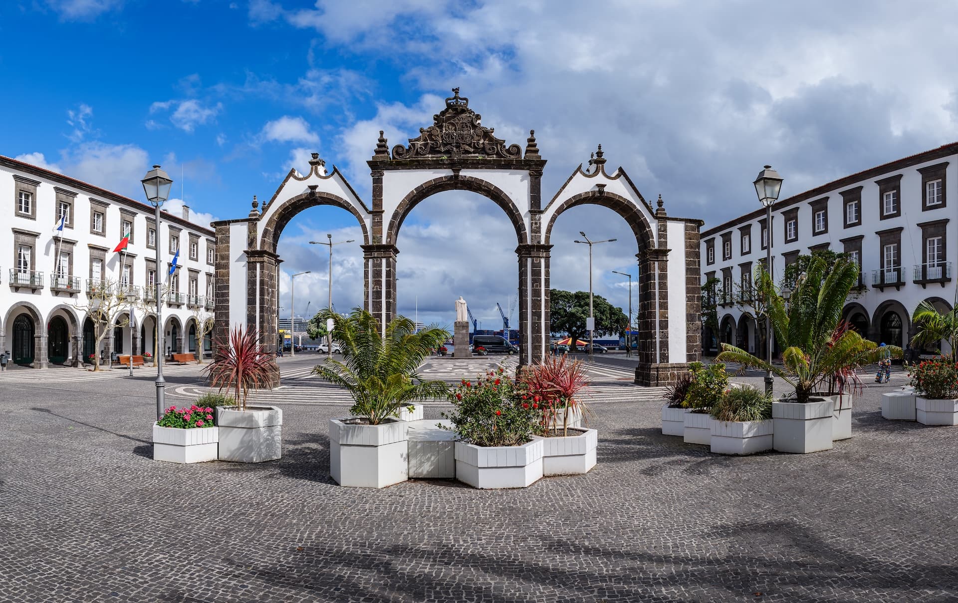 Portas da Cidade arches in a cobblestone square with white buildings and potted plants in Ponta Delgada.