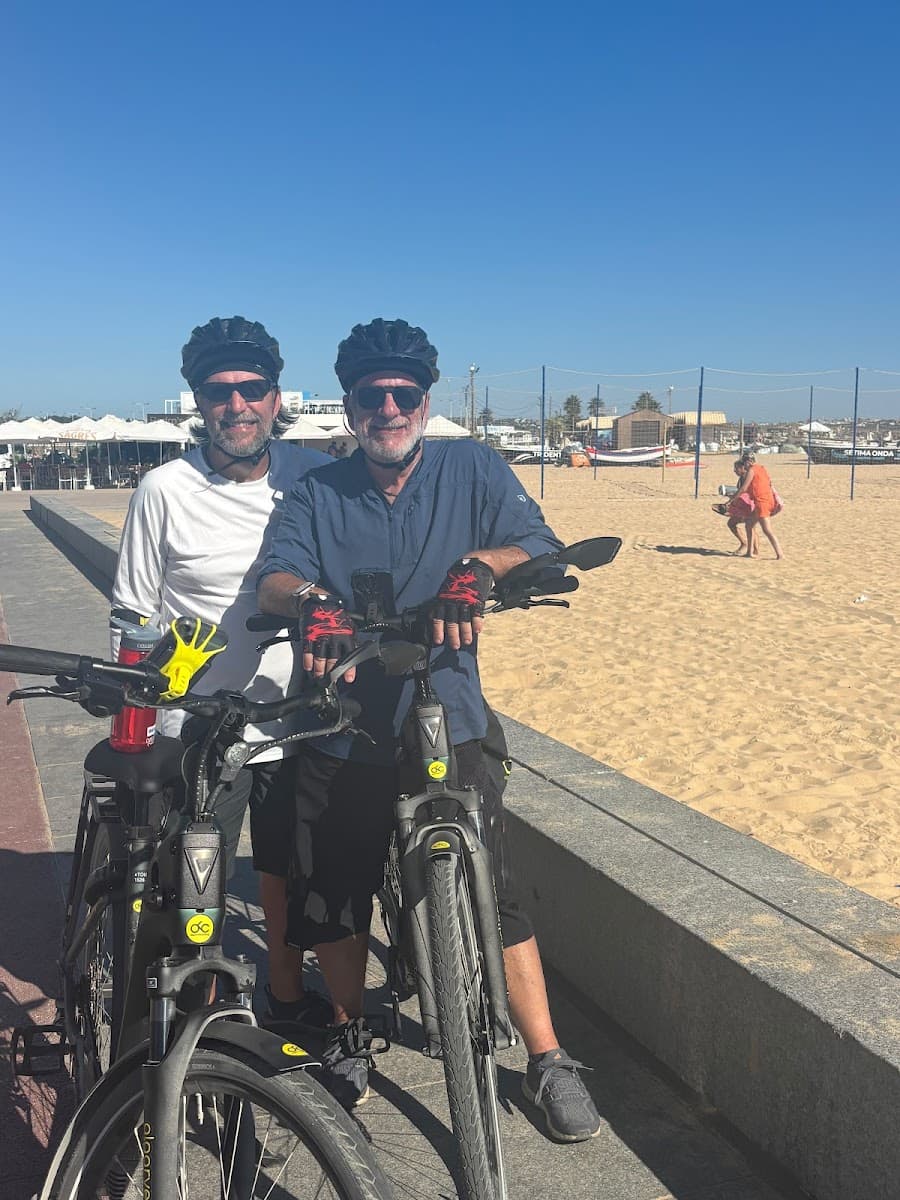 Cyclists standing with electric bikes on coastal promenade near sandy beach