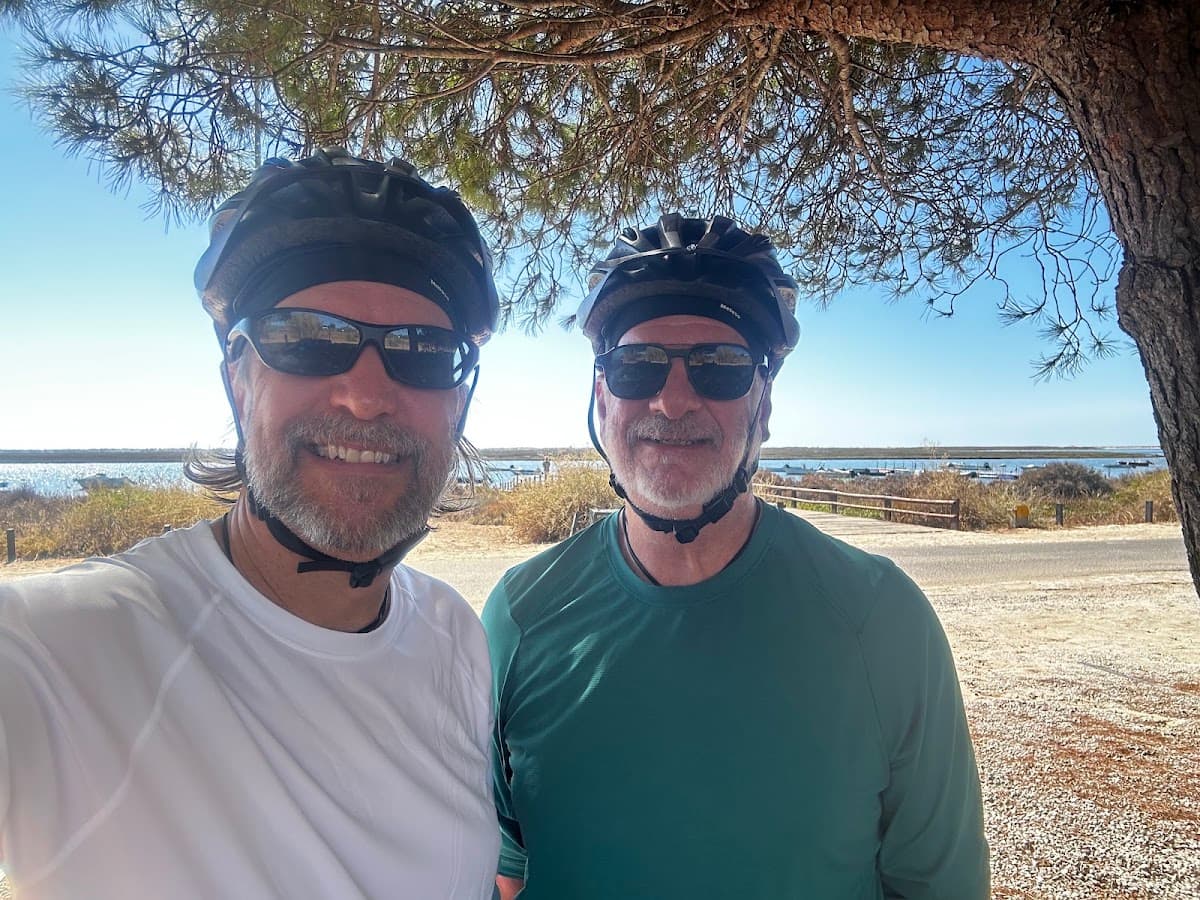 Cyclists wearing helmets and sunglasses posing outdoors by coastal waters